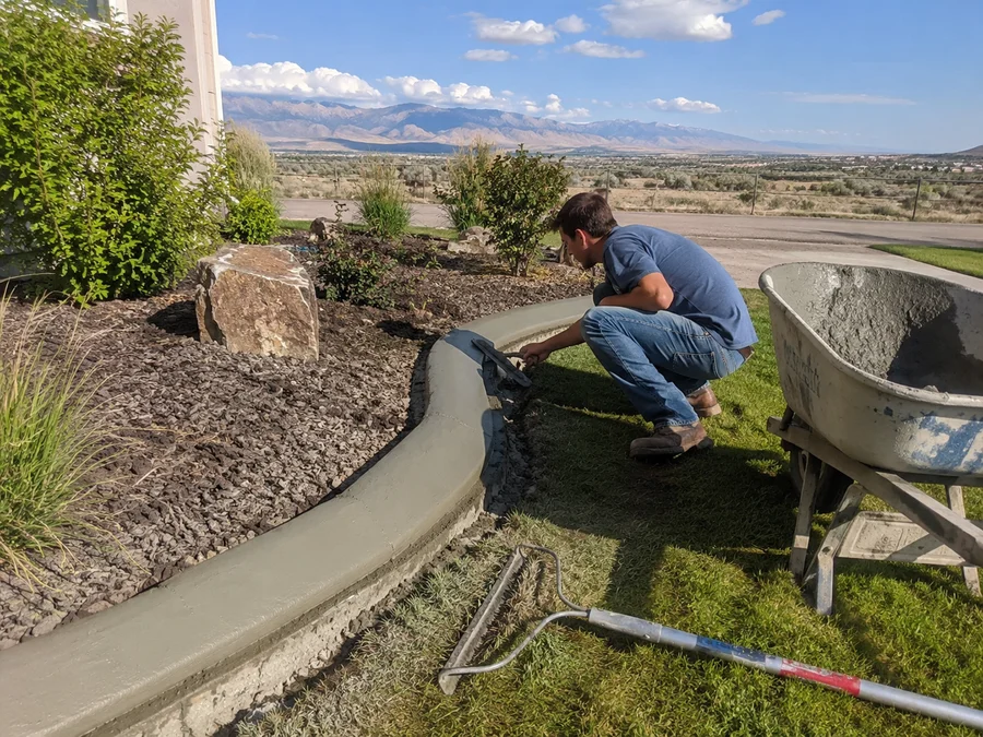 Fresh concrete curbing being finished along a curved garden bed edge