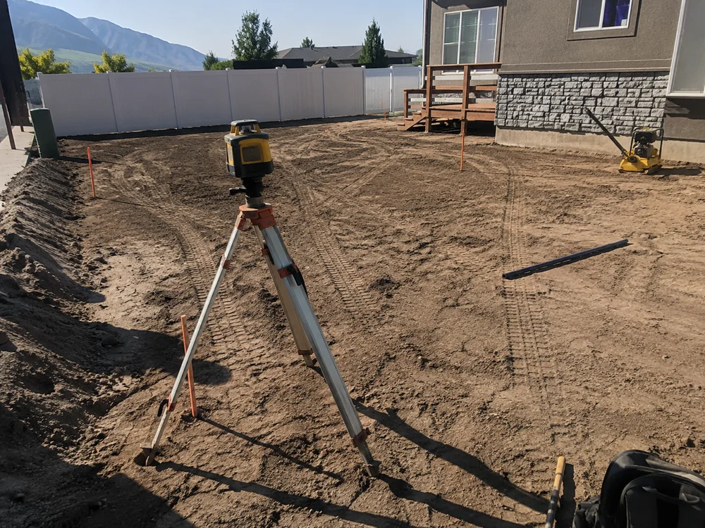 Laser level set up on a tripod in a partly graded Utah yard with grade stakes in the ground