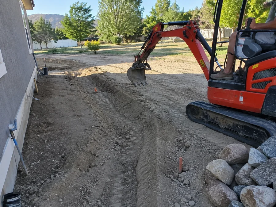 Mini excavator cutting a shallow swale across a Utah back yard to carry runoff away