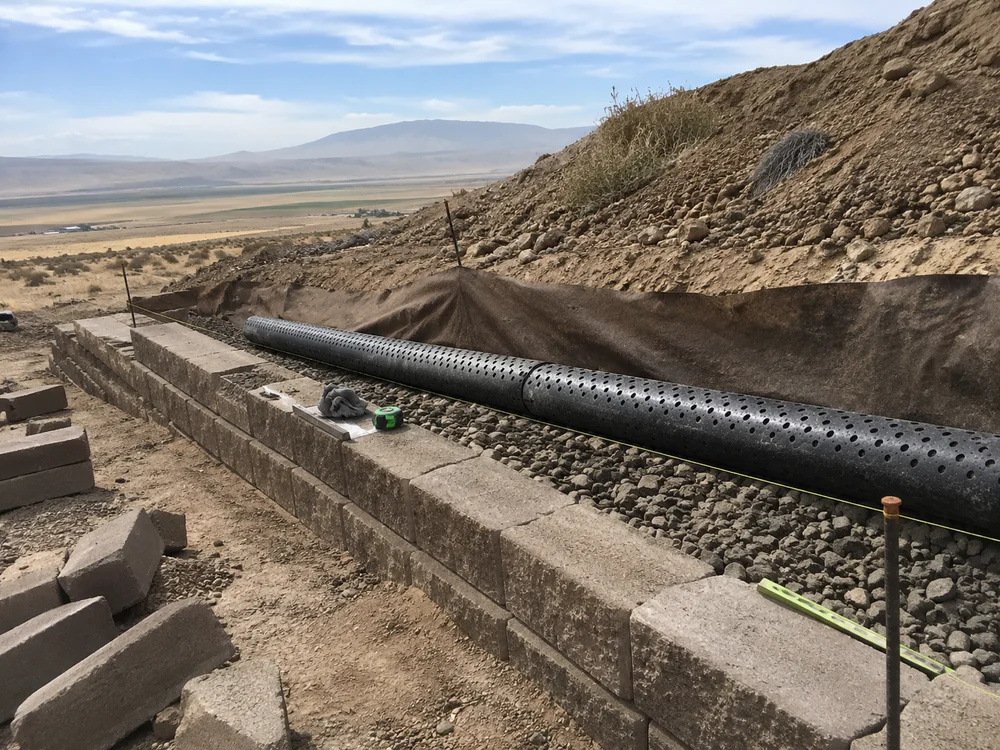 Perforated drain tile laid in clean drain rock behind a retaining wall base course