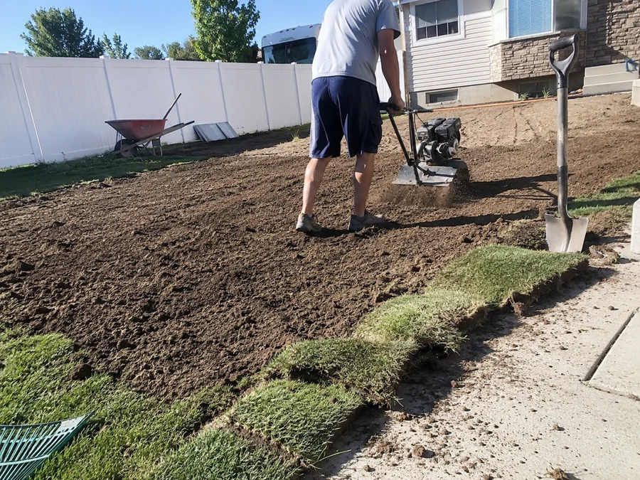 Rototiller working screened topsoil into a prepped lawn area before sod