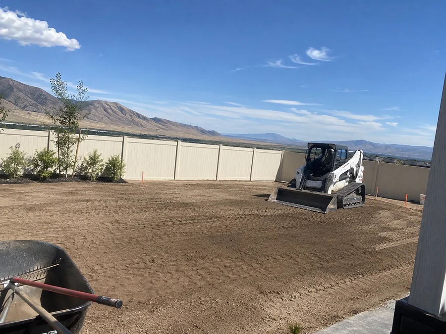 Skid steer finish-grading a new-construction back yard with screened topsoil spread