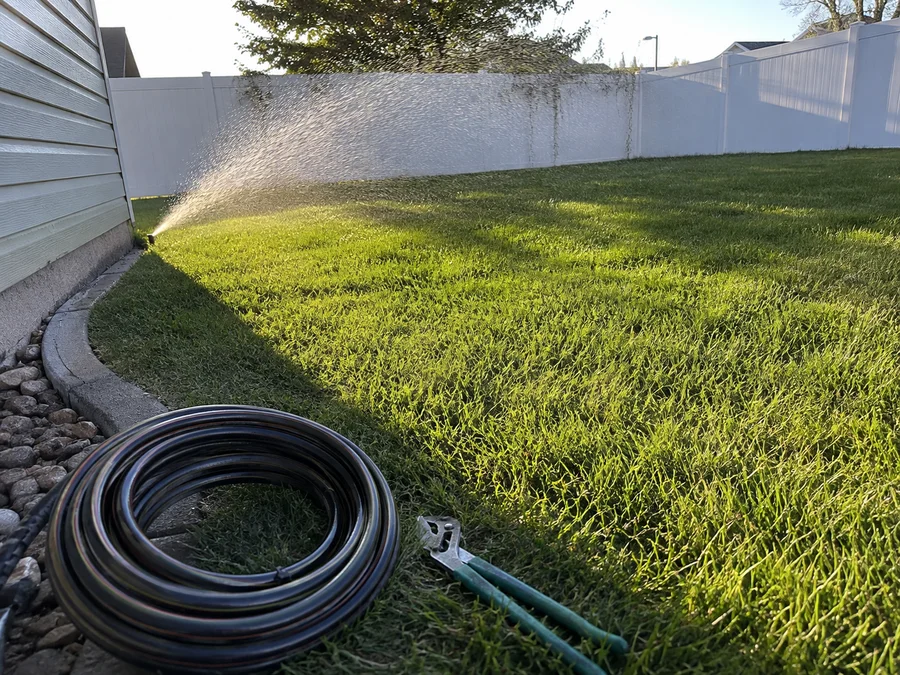 Sprinkler head throwing an even arc across a green Utah lawn in early morning light