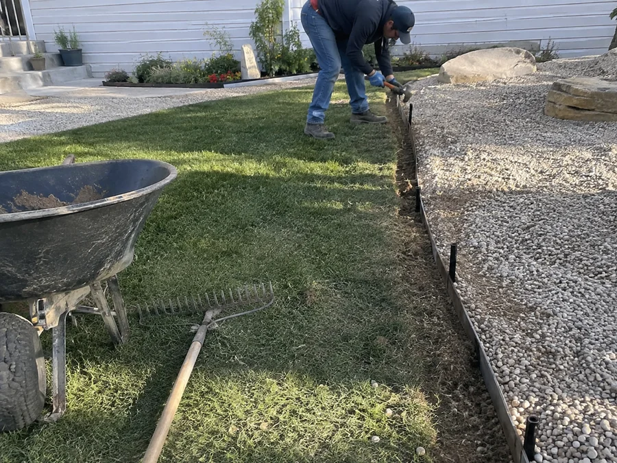 Steel edging being set and staked along a bed line between lawn and gravel