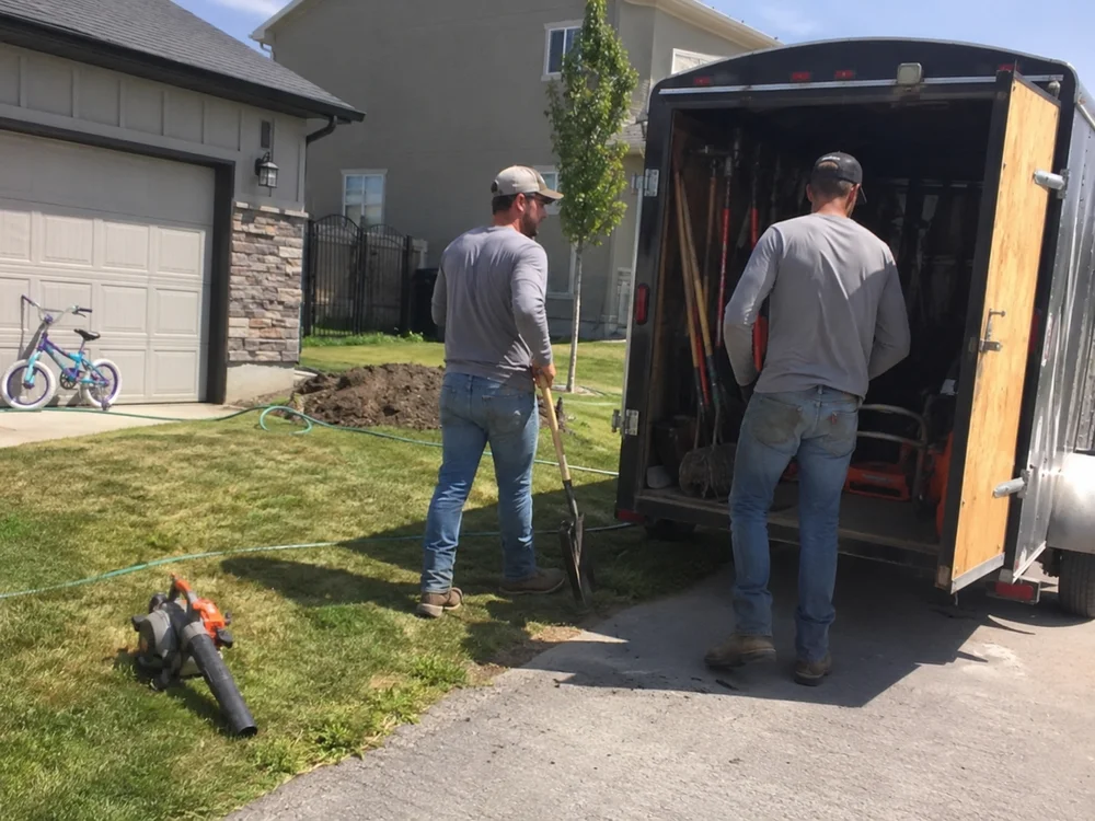 YLC Landscaping crew members loading tools into the work trailer at the end of a job