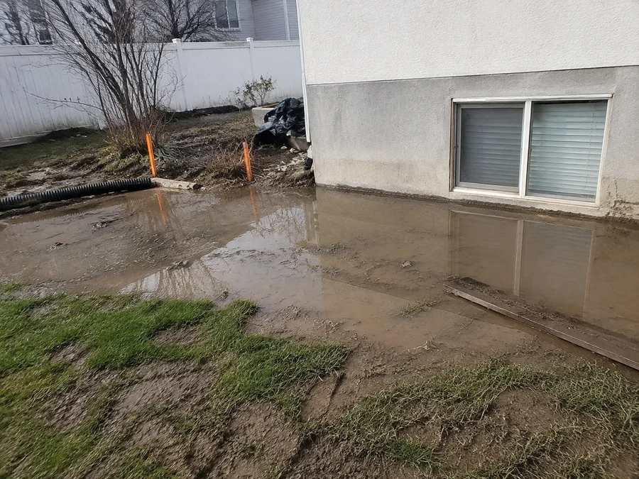 Water pooling against a house foundation in a poorly graded Utah yard after a storm